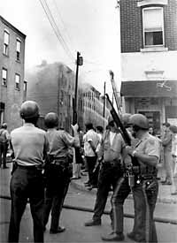 Camden police officers wield shotguns on Cedar Street in North Camden on Aug. 21, 1971 as a building burns in the rear