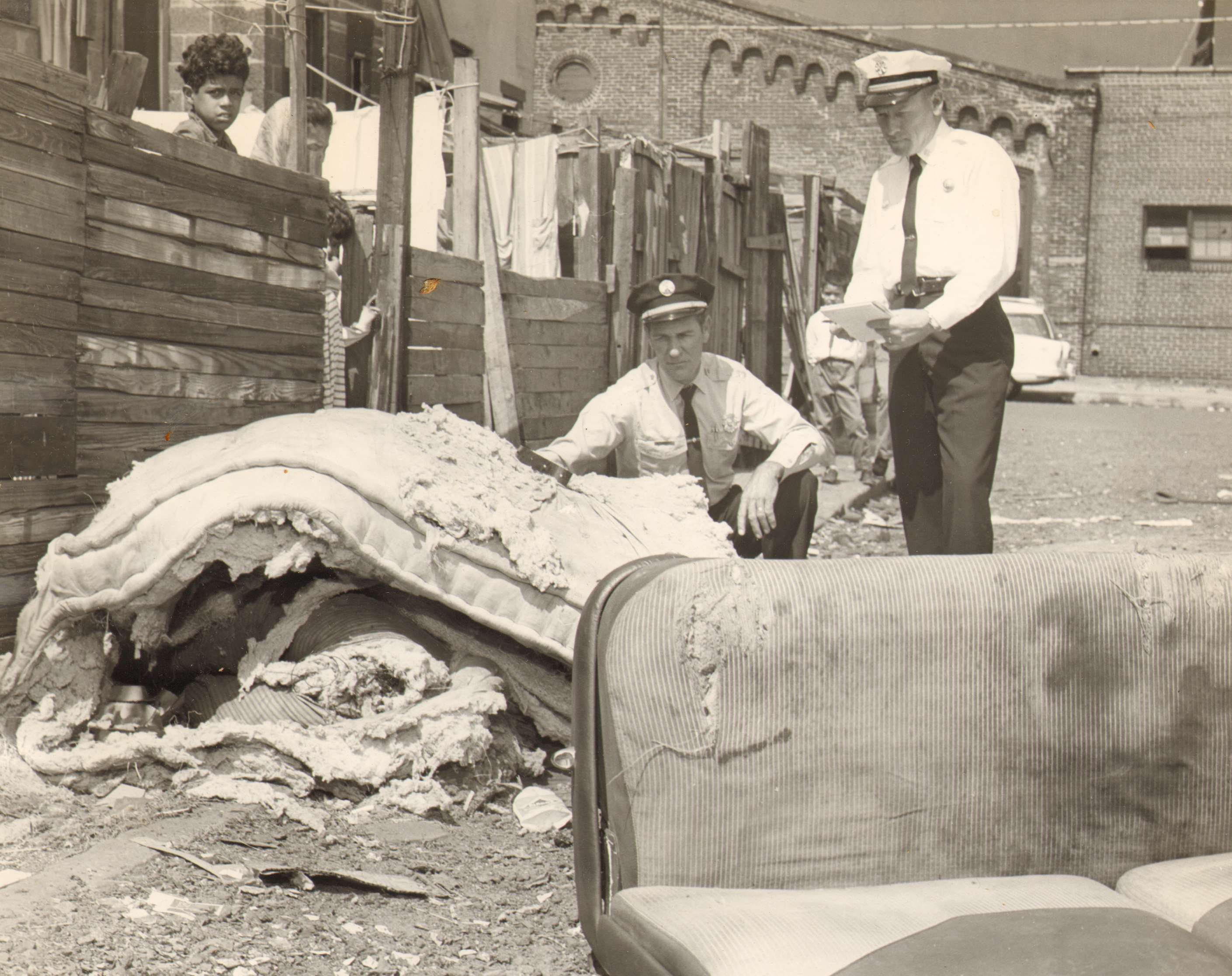 Capt. Charles Bates and Chief George Baxter check pile of discarded bedding at rear of house on Burns St. during cleanup campaign