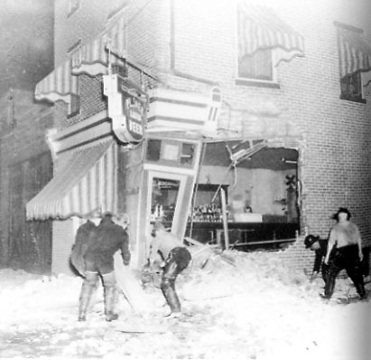 Subsequent damage to tavern following collapse of factory walls, firefighters freeing charged hose line beneath rubble