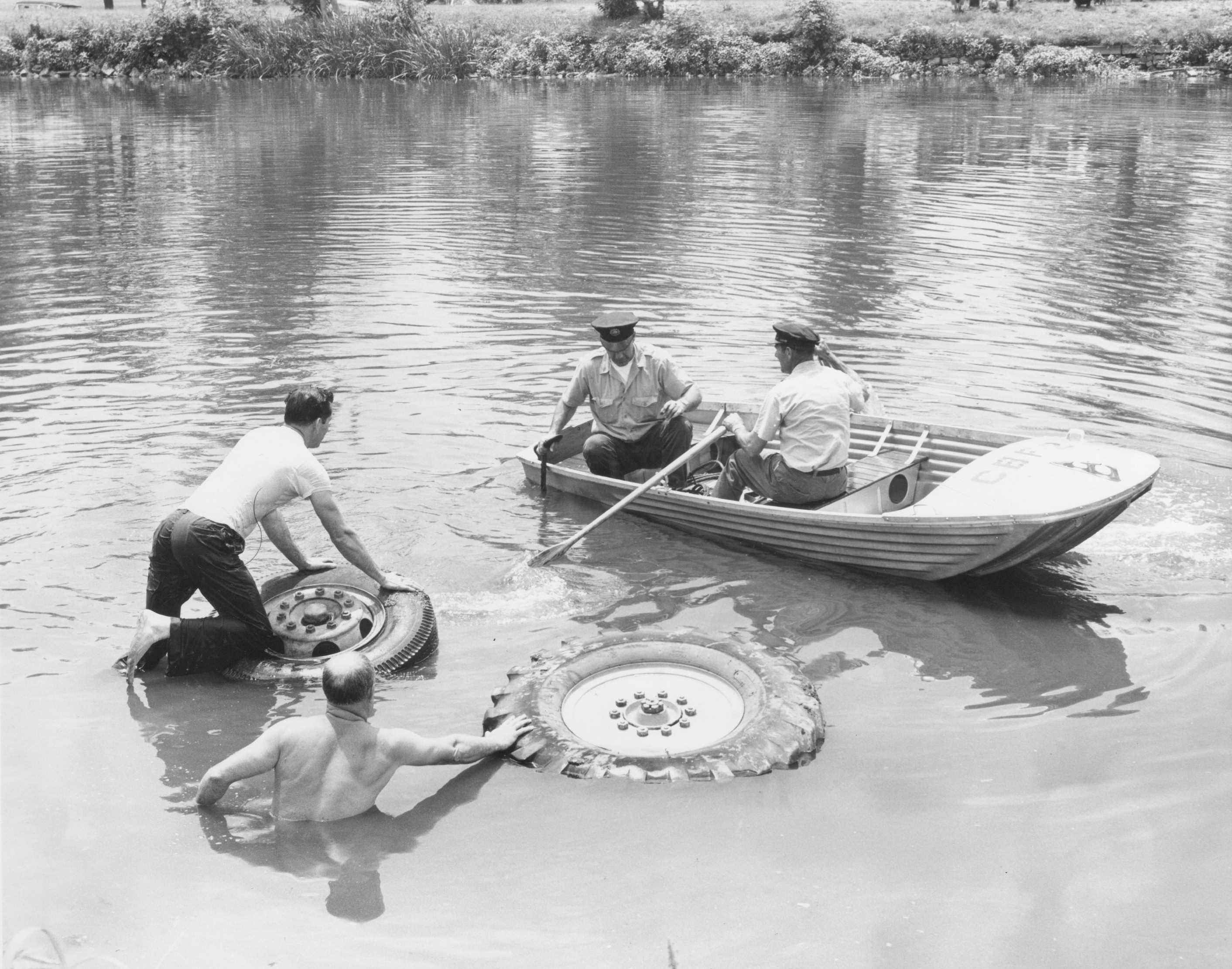 July 18, 1960 industrial accident at the Cooper River at Baird Avenue. Battalion Chief William Deitz without shirt in foreground, Rescue Company 1 members Edward Brendlinger kneeling on machine wheel, John Mogck Jr. and James McGrory in boat.