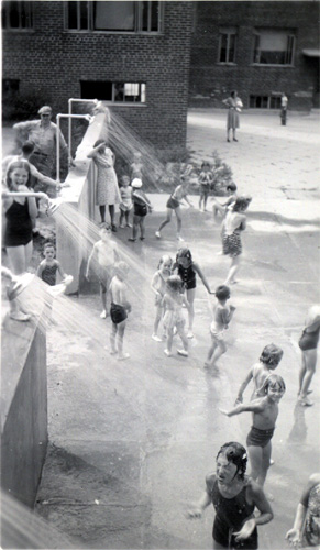 View from the top of concrete platform in front of 346 Dudley Street, showing children paddling in water from showers, July 1940