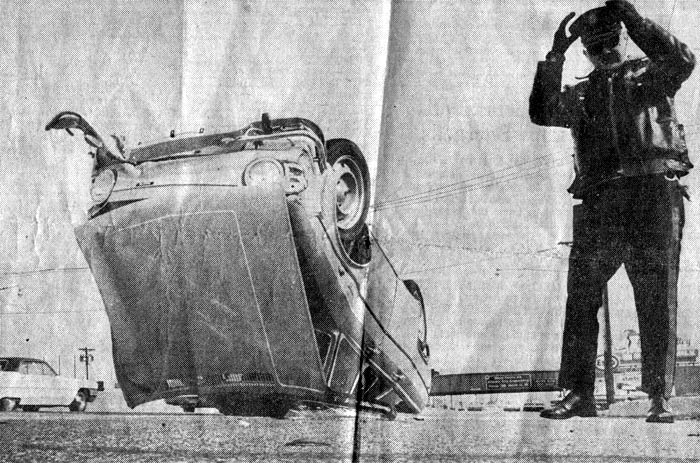 Overturned compact car on Admiral Wilson Boulevard, with Patrolman Edward Eldred reaching for his cap