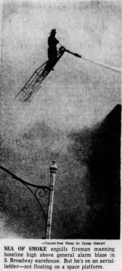 Sea of Smoke engulfs fireman manning hoseline high above general alarm blaze in S. Broadway warehouse on an aerial ladder