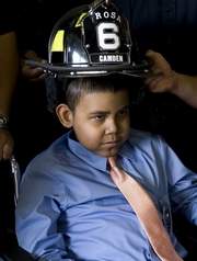 Camden firefighter Pete Perez holds a helmet over 9-year-old Jacob Rosa after Rosa became an honorary junior firefighter — July 1, 2009