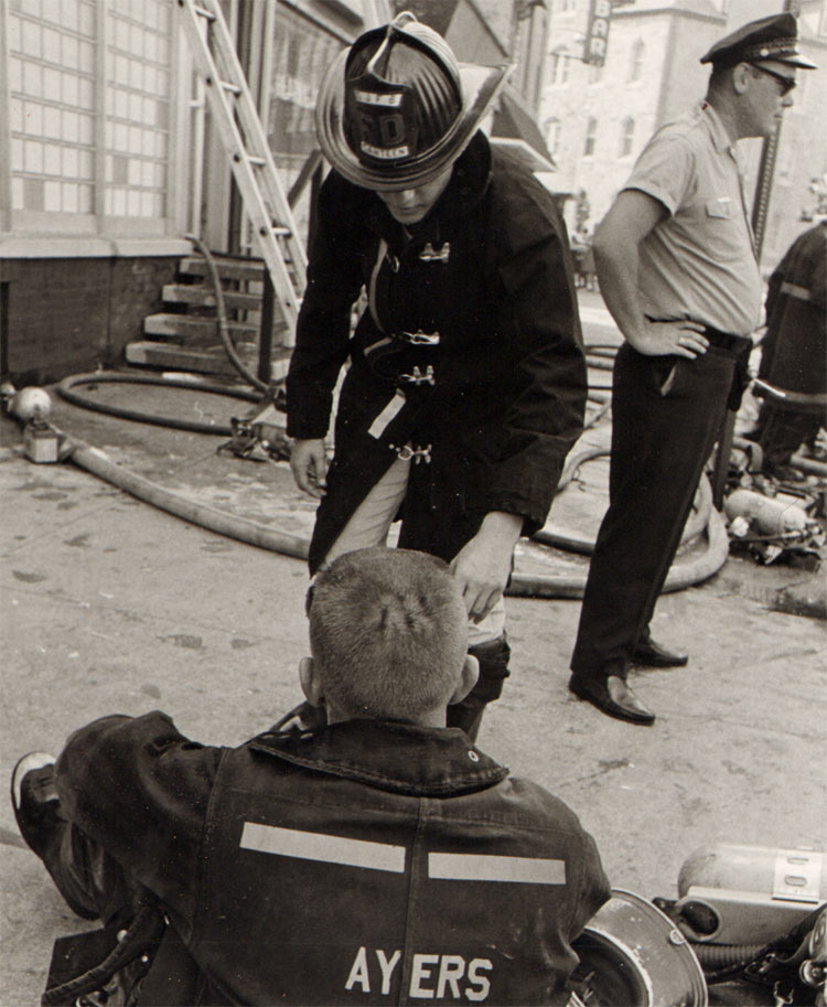 Canteen Corpsman Peter Meyer serves refreshments to Captain William Ayers of Ladder Company 1 after Third Alarm fire, August 14, 1969. Fire Inspector William Neale stands in background.