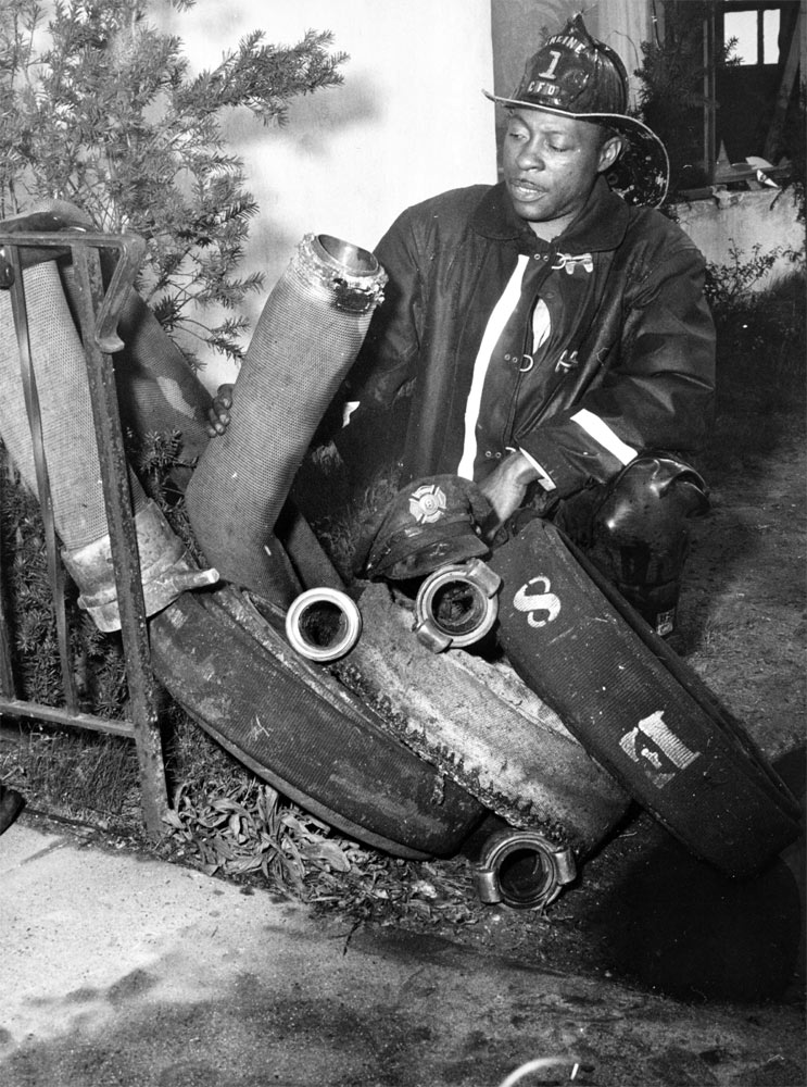 Bob Thomas of Engine Company 1 with burnt hose lengths after a Greater Alarm Fire, 1953